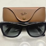 A pair of shiny black Ray-Ban Meta Gen 1 smart glasses positioned in front of their brown leather charging case. (Ray-Ban Meta smart glasses)