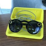 Black Spectacles with a lanyard in a yellow charging case. (Snap Spectacles)